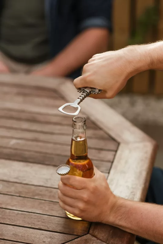 man opening glass bottle of beer with opener