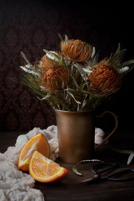 orange flowers in brown vase beside sliced orange fruit
